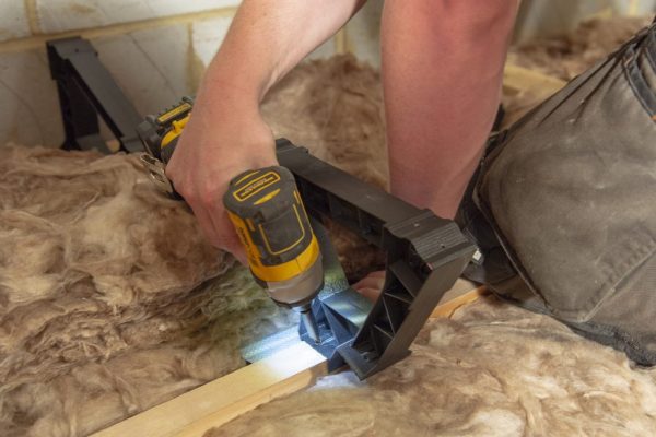 A person using an electric drill with a built in light to install a plastic bracket to a floor.