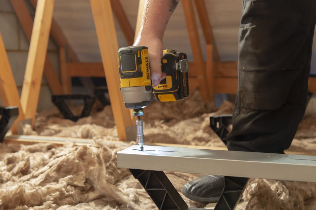 A hand holding a drill and screwing down a floor-heightening bracket.